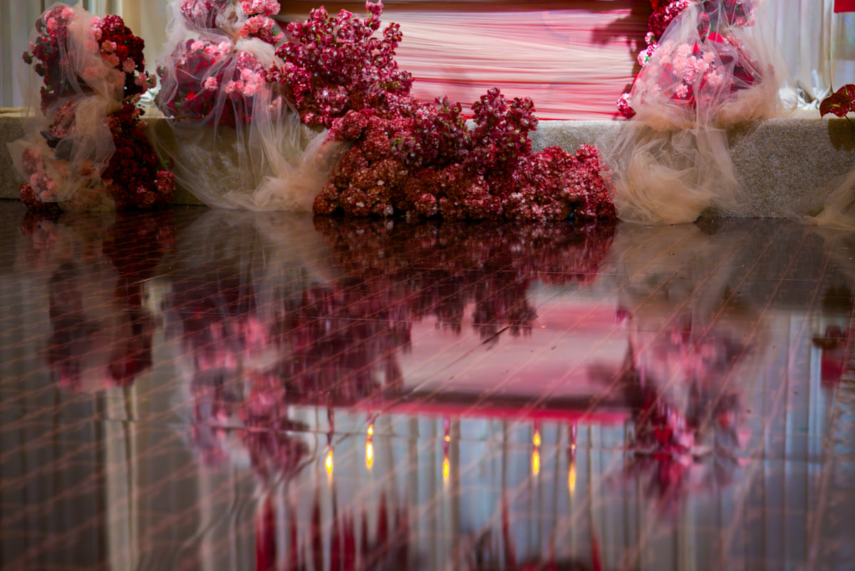 Reflective dance floor with red geometric lines beneath burgundy floral event decorations.
