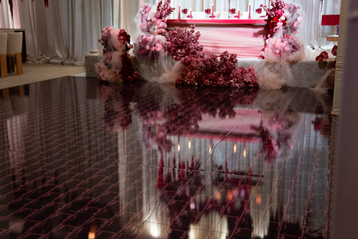 Wide view of a reflective dance floor with red geometric lines and burgundy floral event decorations.
