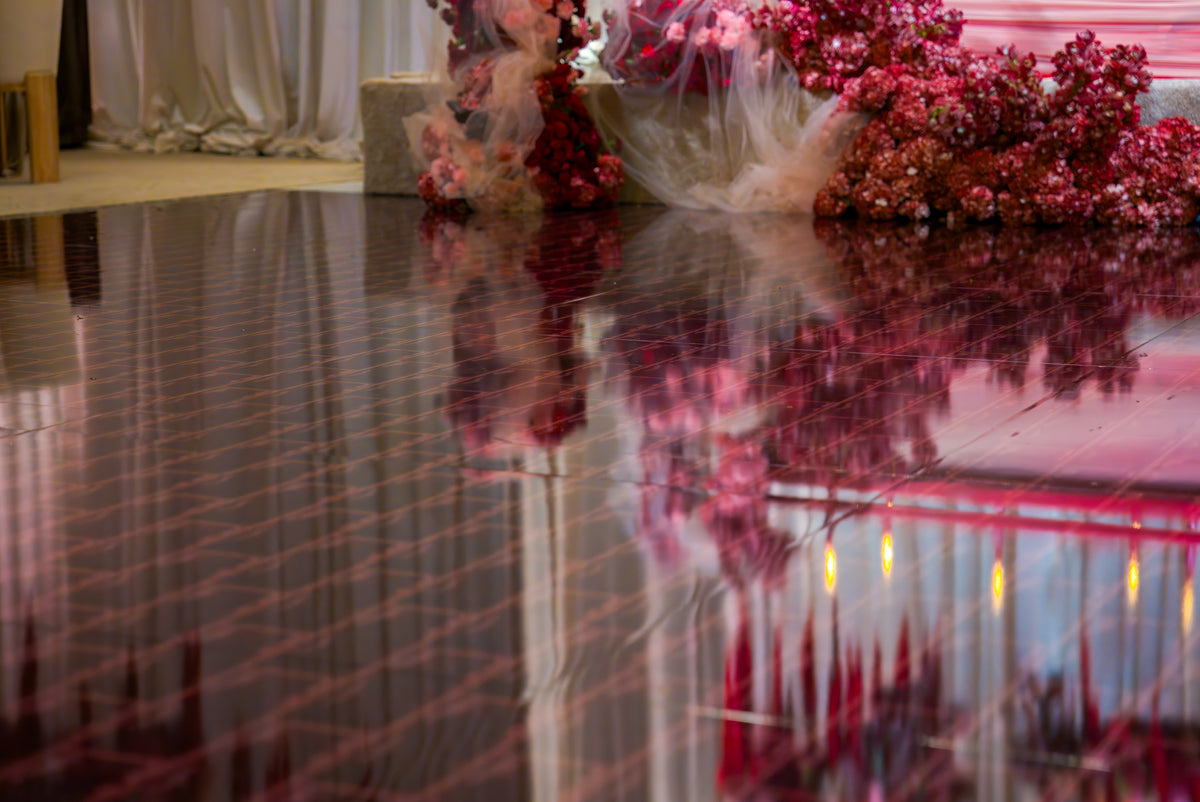 Glossy dance floor with a red geometric pattern reflecting floral decorations and venue lighting.